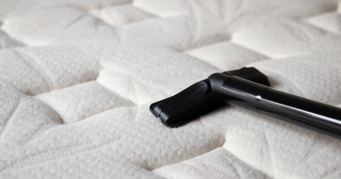 Dust mites in bed — person using a HEPA filter vacuum on a mattress to remove dust mites and allergens.
