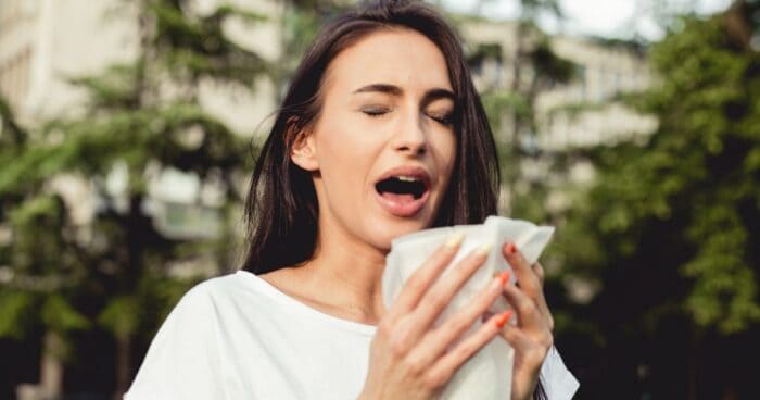 sneezing allergy — Woman sneezing into a tissue, a defensive reaction of the body to irritation.