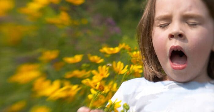 sneezing allergy — Woman sneezing into a tissue outdoors, which may be a symptom of pollen allergy.